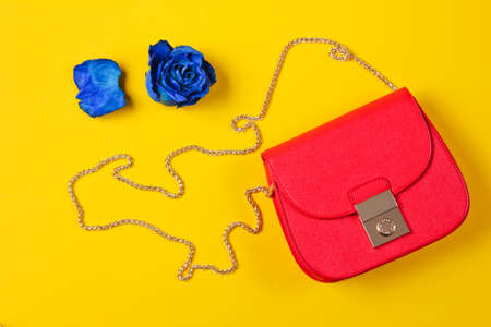 Red leather bag and bud of blue dry rose on yellow background. Top view
