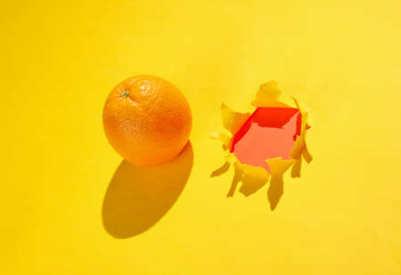 Orange and a torn hole in yellow paper. Minimalistic fruit conceptの写真素材