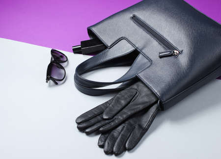 Leather bag, sunglasses, gloves, perfume bottle on gray-purple background. Women's fashion...