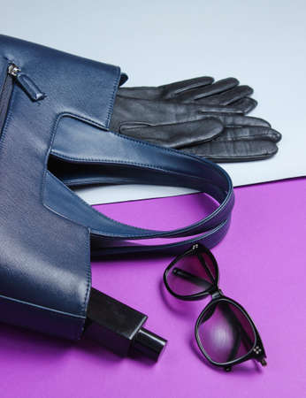 Leather bag, sunglasses, gloves, perfume bottle on gray-purple background. Women's fashion...