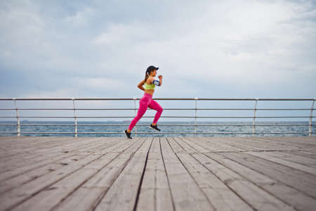 Fit woman in sportswear is running on the beach. Morning running. Healthy lifestyle concept.の写真素材