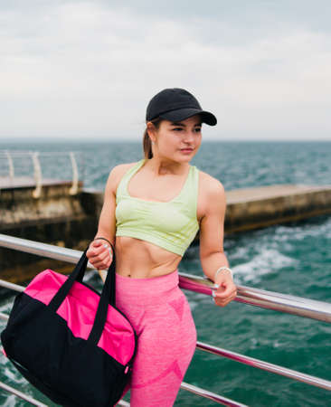 Young athletic woman in sportswear holding a bag for training and posing on the beachの写真素材