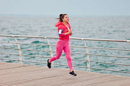 Fit woman in sportswear is running on the beach. Morning running. Healthy lifestyle concept.