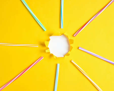 Cocktail tubes on a yellow paper background with a torn hole for copy space. Top view. Minimalism summer conceptの写真素材