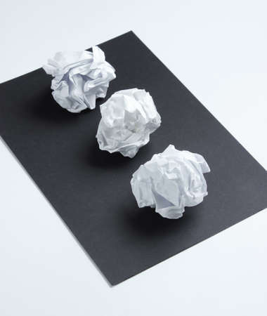 Crumpled paper balls on a black sheet of paper on a white backgroundの写真素材