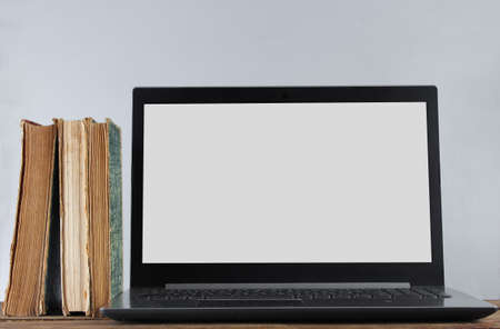 Modern laptop and stack old books  on wooden shelf against the white wall background. Old and new...