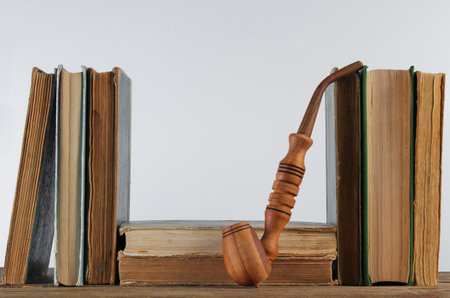 Stack of old books, smoking pipe on wooden shelf against the background of white wallの写真素材