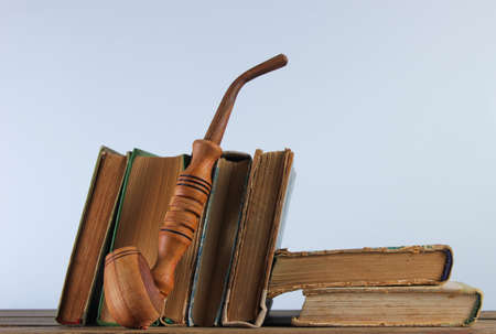 Stack of old books, smoking pipe on wooden shelf against the background of white wallの写真素材
