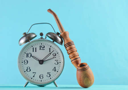 Retro alarm clock and smoking pipe closeup on a blue background.