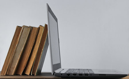 Modern laptop and stack old books  on wooden shelf against the white wall background. Old and new...