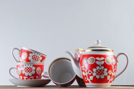Antique ceramic cups and teapot on wooden table against a white wallの写真素材