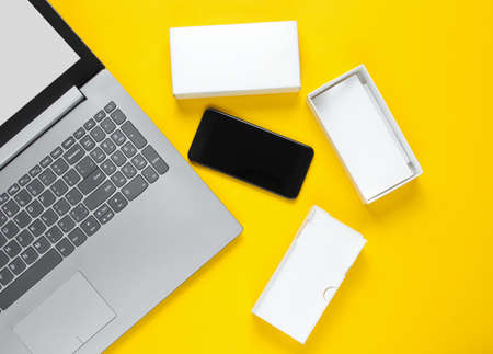 The concept of unboxing, techno blogging. Box with a new smartphone, laptop on yellow background.