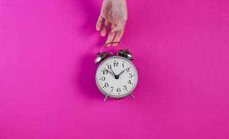 Female hands hold retro alarm clock on pink backgroundの写真素材