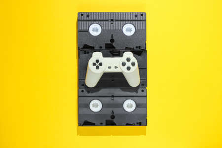 Gamepad on retro video cassettes. Minimalism studio shot on yellow background