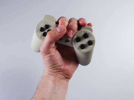 Male hand holding gamepad over gray background.