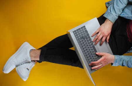 Online worker concept. Hipster man typing on laptop and sits on yellow background. Studio shot. Top viewの写真素材