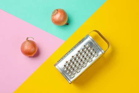 Old grater and onion bulbs on pastel background. Top view. Minimalistic food concept