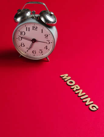 Retro alarm clock on red background with text morning with letters.