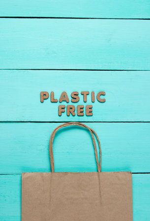 Paper bag on blue wooden background with the words plastic free. Top view