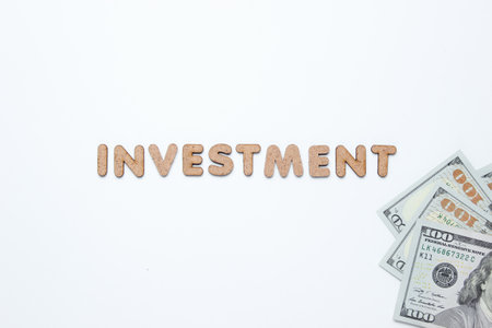 Word investment and dollar bills on a white background. Top viewの写真素材