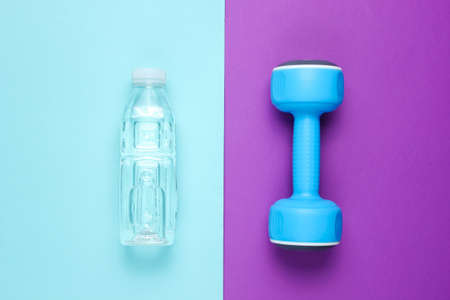 Minimalistic fitness concept. Dumbbell, bottle of water on colored background. Top view