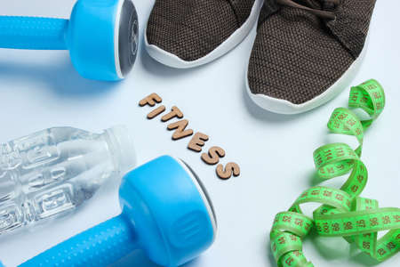 Healthy lifestyle. Dumbbells, ruler,  bottle of water, sneakers on gray background with word...