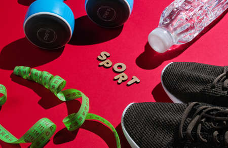 Healthy lifestyle. Dumbbells, ruler,  bottle of water, sneakers on red background with word sport. Slimming concept.の写真素材