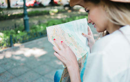 Blonde woman in a felt hat looks at city map in unfamiliar city outdoor