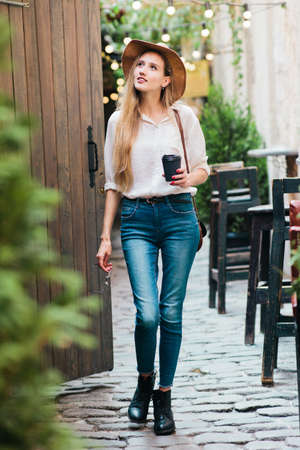 Young attractive woman in casual style clothes walking along the courtyard of the old city with a...