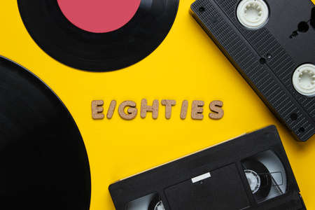 Retro style concept, 80s. Video cassette and vinyl records on yellow background with the word...