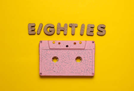 Creative retro style concept, 80s. Audio cassette on yellow background with the word Eighties from...