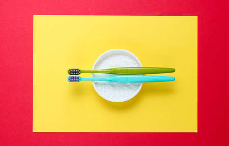 Two toothbrushes, tooth powder on yellow red background. Minimalism oral hygiene concept. Top view