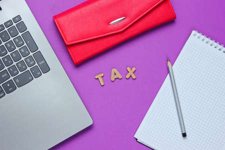 Creative flat lay business concept. Laptop, notebook with a pencil, wallet on a purple background with the word tax of wooden letters. Top view, minimalismの写真素材