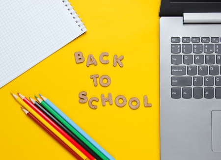 Back to school minimalistic concept. Laptop, color pencils, notebook on yellow background. Slogan...