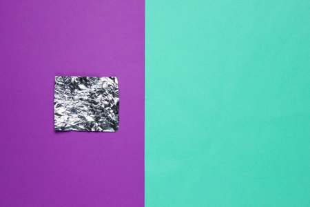 A piece of foil on colored paper background. Top view. Minimalism concept