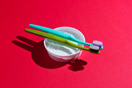 Two toothbrushes, tooth powder on red background. Minimalism oral hygiene concept.の写真素材
