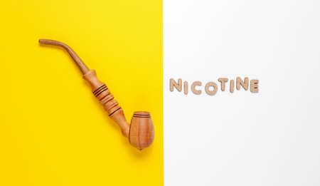 Wooden smoking pipe on white yellow background with word nicotine of wooden letters. Top viewの写真素材