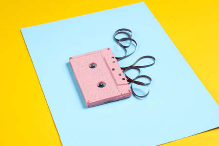 Music lover minimalism concept. Retro style 80s. Pink audio cassette with film on a blue yellow paper background.の写真素材