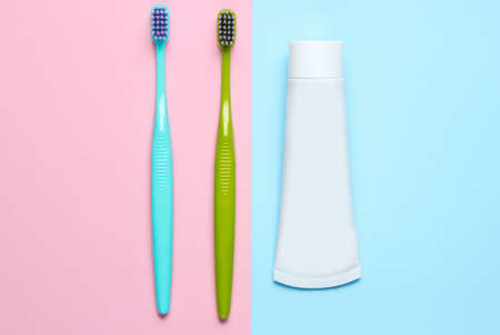 Two toothbrushes with a tube of toothpaste on pastel background. Top view