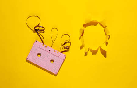 Music lover minimalism concept. Retro style 80s. Pink audio cassette with film on yellow paper background with torn hole.の写真素材