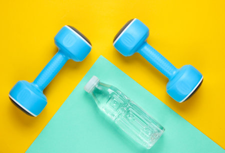 Minimalistic sport concept. Blue plastic dumbbells, bottle of water on colored paper background. Top viewの写真素材