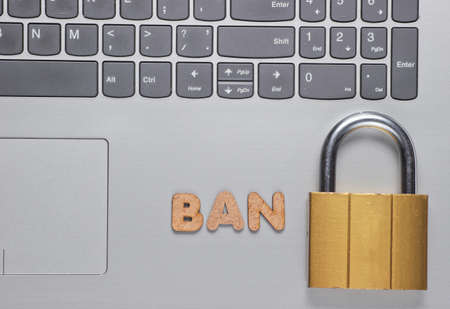 Ban account. Lock on laptop keyboard with the word ban of wooden letters