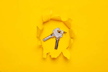 Bunch of metal keys through a torn hole on a yellow paper backgroundの写真素材