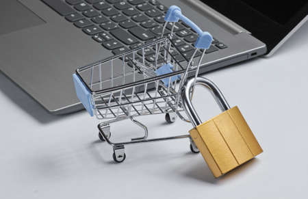 Restriction on online shopping minimalistic concept. Mini shopping trolley with lock, laptop on white backgroundの写真素材