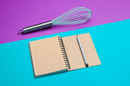 Minimalism cooking concept. Recipe book, whisk on a blue-purple background.の写真素材