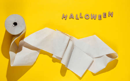 Halloween minimal concept. A roll of toilet paper on yellow background with the word halloween. Top...