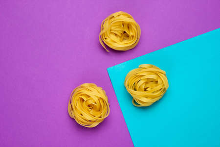 Minimalism italian food concept. Raw tagliatelle noodles on a blue-purple backgroundの写真素材