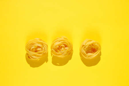 Raw dry tagliatelle noodles on yellow background. Minimalism food conceptの写真素材