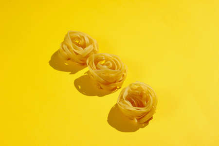 Raw dry tagliatelle noodles on yellow background. Minimalism food conceptの写真素材