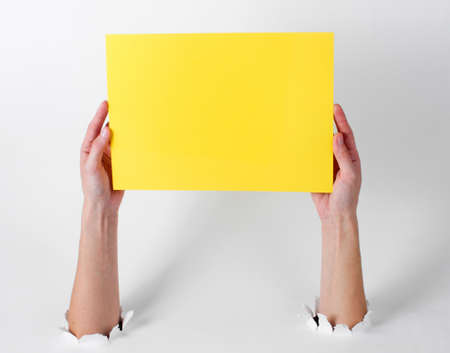 Female hands holding yellow sheet of paper for copy space through the torn holes of a white background. Creative artの写真素材
